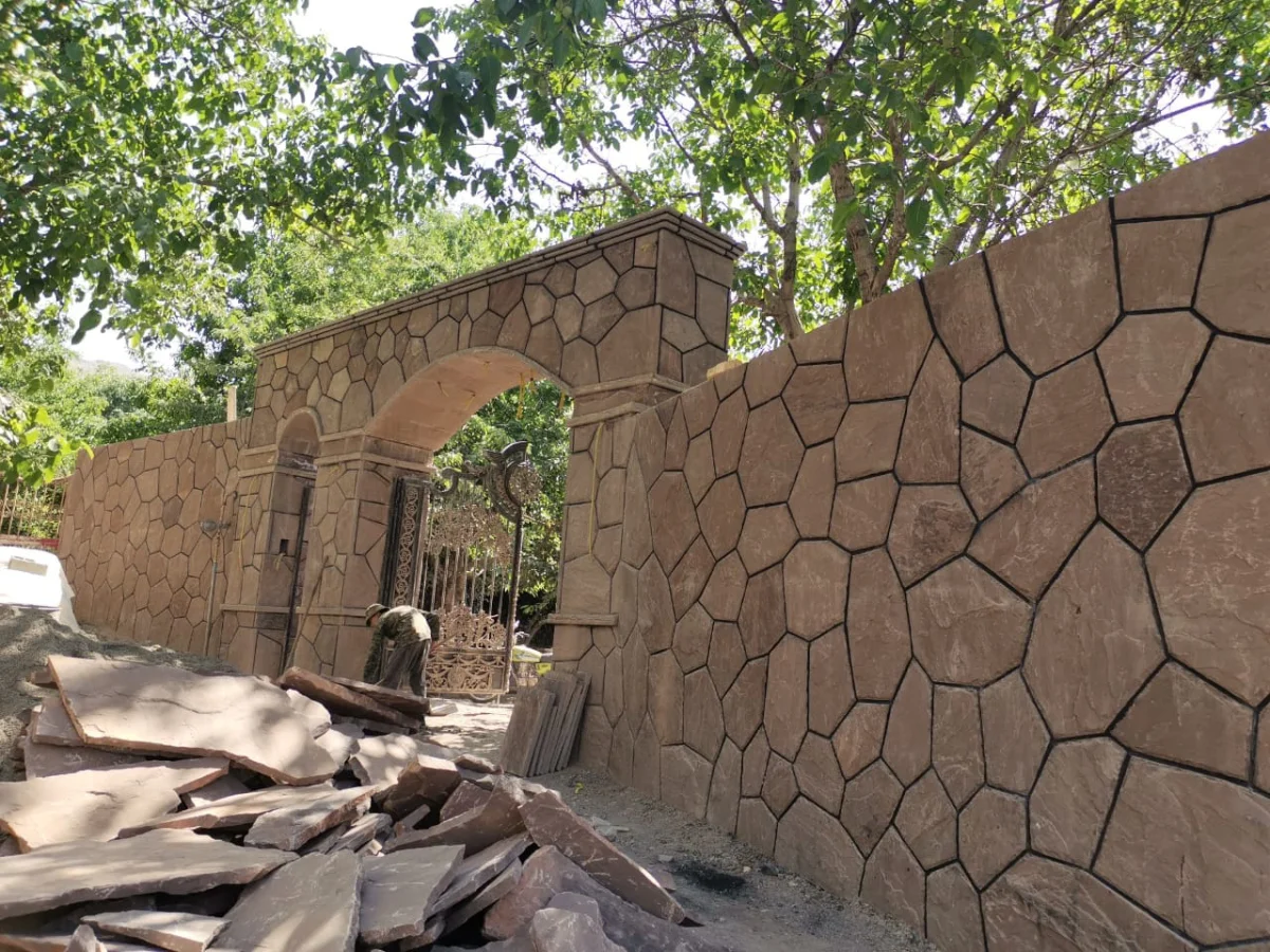 نمایی از یک دیوار حائل بلند و مقاوم با سنگ لاشه خاکستری تیره، استحکام و زیبایی در کنار هم.